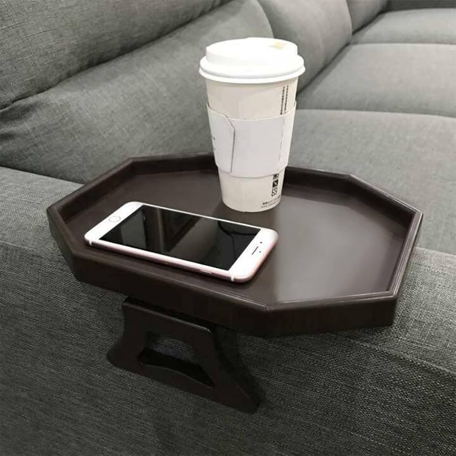 A small octagonal or polygonal tray in dark brown is clamped to the sofa arm, supporting a coffee cup and phone.